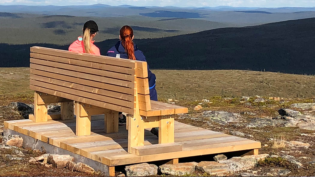 两个女人背坐在木凳上。女人们此时在观看的山景。