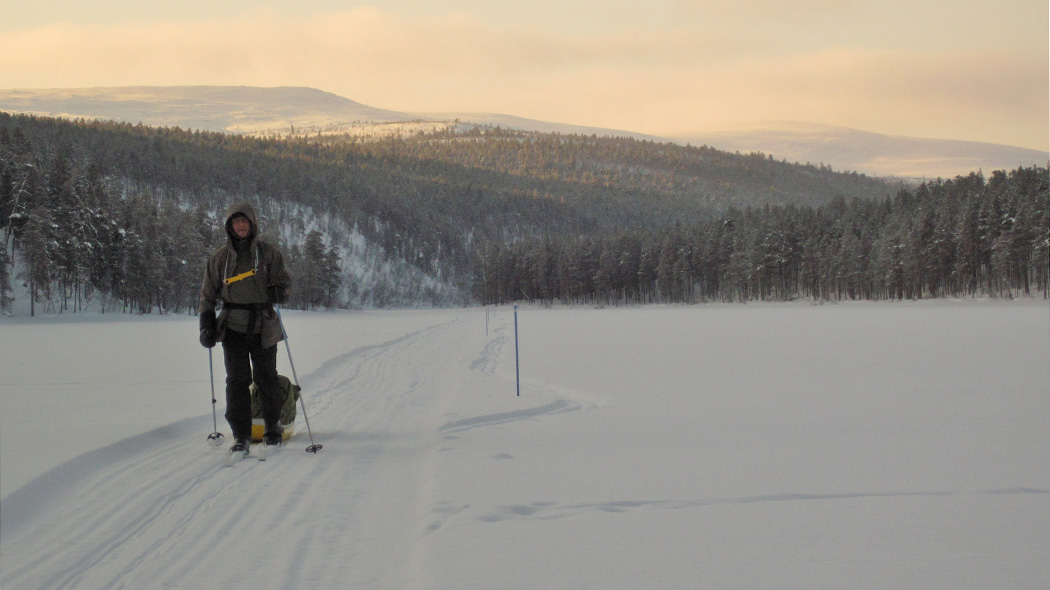 男子沿着雪地摩托小路，在平坦的道路上滑雪并带有甩尾动作。背景中有山丘。
